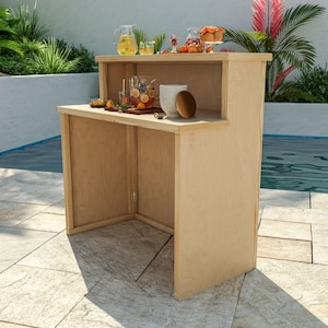 May include: A light-coloured wooden outdoor bar with two levels. The top level holds jugs of drinks, glasses, and fruit. The lower level has a large mug and a tray of food. The bar is set up near a swimming pool.
