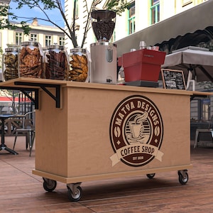 Puede incluir: Un carrito de cafeter&iacute;a m&oacute;vil con acabado de madera clara, con un molinillo de caf&eacute;, una m&aacute;quina de espresso y frascos de vidrio llenos de galletas. El carrito tiene el logotipo "Matua Designs Coffee Shop" y est&aacute; sobre ruedas.
