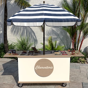 May include: A white and beige charcuterie cart with a blue and white striped umbrella. The cart has a wooden countertop with various food items and a round sign that says "Charcuterie". The cart is on wheels.