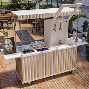 May include: A white and wood-toned outdoor beverage cart with a striped awning. The cart has a built-in dispenser, serving area, and a sign that reads "Special Drinks". The cart is on wheels and is set up on a brick patio.