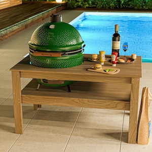 Può includere: Un barbecue verde Big Green Egg è su un tavolo di legno, con vino, condimenti e hamburger. Il tavolo è vicino a una piscina, suggerendo una cucina all'aperto. Il barbecue ha il testo "Big Green Egg".