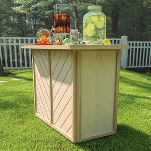 May include: A light wood outdoor bar with a chevron design on the front panel. The bar is set on a green lawn and is topped with beverage dispensers and glasses filled with fruit and drinks.