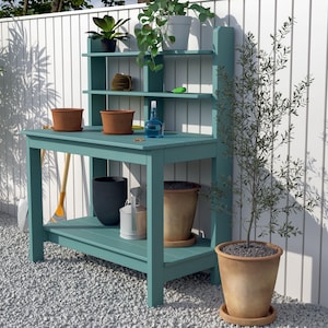 Puede incluir: Un banco de jardinería turquesa con un estante y un respaldo, que contiene plantas en macetas y herramientas de jardinería. El banco tiene un estante inferior y está sobre un lecho de grava. Un pequeño árbol en una maceta de terracota está a la derecha.