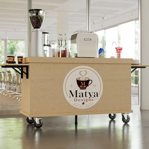 May include: A light wood-toned coffee cart on wheels, featuring a coffee grinder, espresso machine, and coffee cups. The cart has a circular logo with a coffee cup and the text "Matya Designs". The cart is in a bright, modern space.
