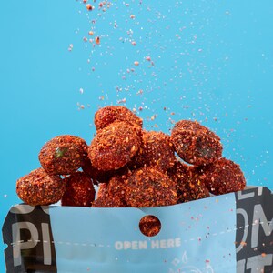 Puede incluir: Una bolsa azul con las palabras "Mr. Picante" impresas en ella. La bolsa está llena de caramelos gomosos rojos y picantes. Los caramelos se derraman de la bolsa sobre un fondo azul.