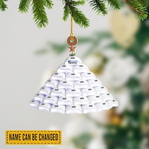 May include: A white Christmas tree ornament with the text "Name" at the top. The ornament is made of small white objects arranged in a triangular shape. The ornament hangs from a gold string.