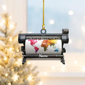 May include: A black and gray ornament shaped like a large format printer, with a colorful world map design on the paper roll. The word "Name" is printed in white on the paper. The ornament hangs from a gold string.
