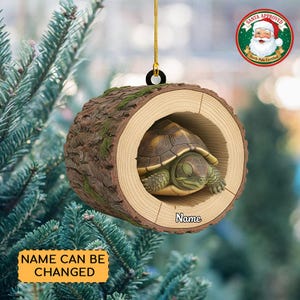 May include: A Christmas ornament featuring a turtle inside a log cabin design. The ornament is brown with green moss accents and a gold hanging string. The text "Name can be changed" is on a yellow banner.