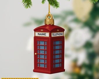 May include: A red Christmas ornament shaped like a British telephone box, with the words "NAME" and "TELEPHONE" on the top. The ornament has blue window panels and a gold-colored top. The text "NAME CAN BE CHANGED" is on a yellow banner.