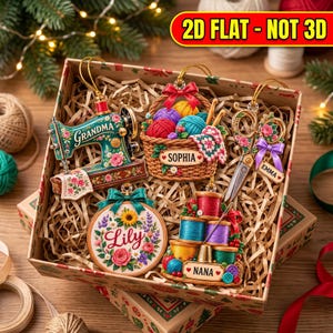 Puede incluir: Un conjunto de cinco adornos planos decorativos en una caja de regalo. Los adornos incluyen una m&aacute;quina de coser con la etiqueta 'Grandma', una cesta de lana 'Sophia', unas tijeras 'Emma', un bastidor de bordado 'Lily' y carretes de hilo 'Nana'.