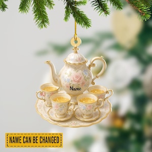 May include: A decorative ornament featuring a miniature tea set. The set includes a teapot, four teacups, and saucers, all adorned with floral patterns in pink and blue. The text "Name" is printed on the teapot. The text "NAME CAN BE CHANGED" is printed on a yellow rectangle.