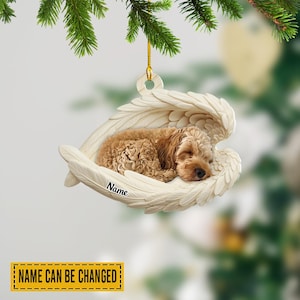 May include: A cream-colored angel wings ornament cradles a sleeping, light brown dog. The ornament hangs from a gold string and has the word "Name" printed on it. The text "NAME CAN BE CHANGED" is in a yellow rectangle.