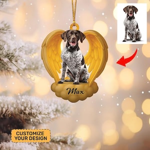 May include: A personalized dog ornament featuring a German Shorthaired Pointer with brown and white markings, set against golden angel wings. The dog's name, "Max," is scripted on a cloud-shaped base. The ornament hangs from a gold cord.