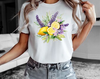 May include: White t-shirt featuring a watercolor design of lemons, lavender, and purple flowers. The design includes two whole lemons and a sliced lemon, with green leaves and lavender sprigs. The shirt is a short-sleeved crew neck.