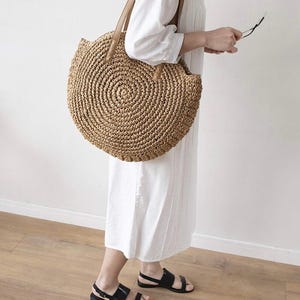 Pu&ograve; includere: Una grande borsa tote rotonda in paglia con manici in pelle marrone. La borsa &egrave; realizzata in paglia intrecciata e ha un aspetto naturale e rustico.