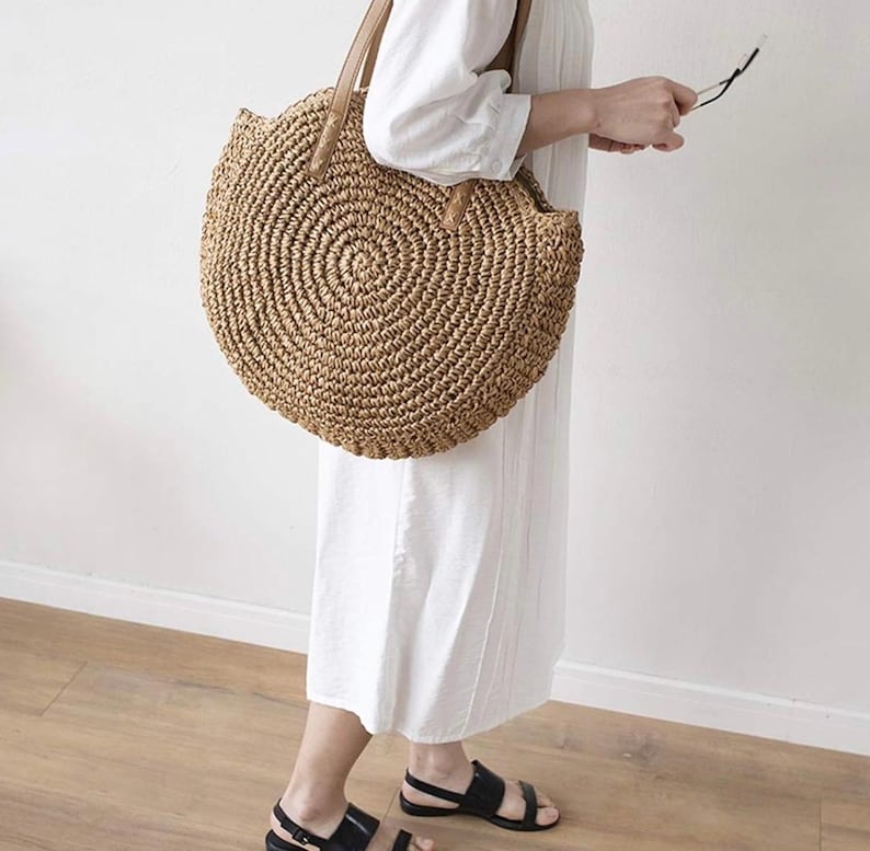 Pu&ograve; includere: Una grande borsa tote rotonda in paglia con manici in pelle marrone. La borsa &egrave; realizzata in paglia intrecciata e ha un aspetto naturale e rustico.