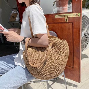 Pu&ograve; includere: Una grande borsa tote rotonda di paglia marrone con manici in pelle. La borsa &egrave; realizzata in paglia intrecciata e ha una forma circolare.