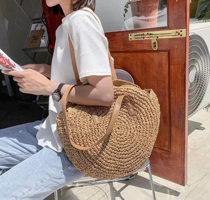 Pu&ograve; includere: Una grande borsa tote rotonda di paglia marrone con manici in pelle. La borsa &egrave; realizzata in paglia intrecciata e ha una forma circolare.