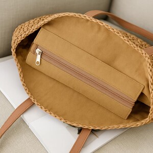 Pu&ograve; includere: Una borsa tote in paglia intrecciata marrone con un manico in pelle marrone e una tasca con cerniera all'interno. La borsa &egrave; foderata con un tessuto marrone.