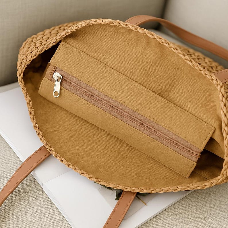 Pu&ograve; includere: Una borsa tote in paglia intrecciata marrone con un manico in pelle marrone e una tasca con cerniera all'interno. La borsa &egrave; foderata con un tessuto marrone.