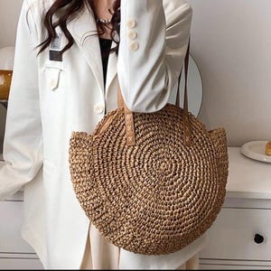 Pu&ograve; includere: Una borsa tote rotonda in paglia con manici in pelle marrone. La borsa &egrave; intrecciata con un motivo circolare e ha una forma leggermente arrotondata.