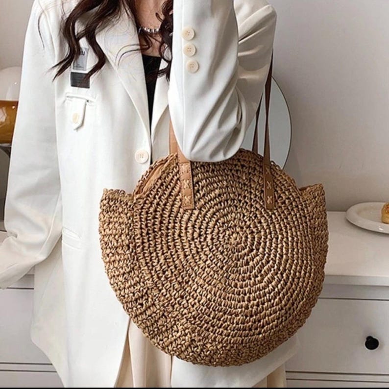Pu&ograve; includere: Una borsa tote rotonda in paglia con manici in pelle marrone. La borsa &egrave; intrecciata con un motivo circolare e ha una forma leggermente arrotondata.