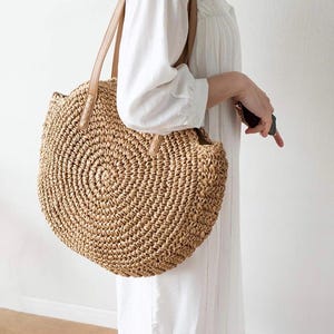 Pu&ograve; includere: Una grande borsa tote rotonda in paglia intrecciata con manici in pelle marrone. La borsa &egrave; realizzata in paglia naturale e presenta un motivo circolare.