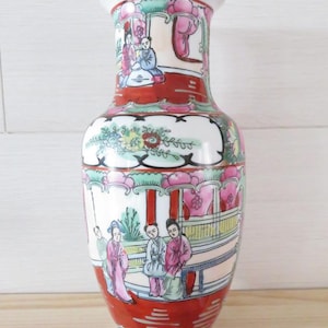 Peut inclure: Un vase décoratif en porcelaine, de couleur blanche, rouge et dorée. Il présente des scènes peintes à la main de personnages en costumes traditionnels. Le design comprend des éléments floraux et architecturaux, créant une esthétique détaillée et ornée.