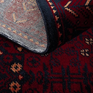 May include: A rolled-up area rug with a deep red background and intricate dark blue and gold patterns. The rug's edge is a dark blue border, and the design features geometric and floral motifs. The rug's texture is visible, suggesting a woven construction.