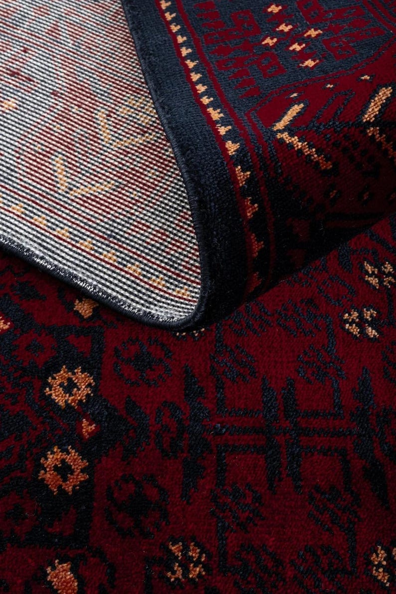 May include: A rolled-up area rug with a deep red background and intricate dark blue and gold patterns. The rug's edge is a dark blue border, and the design features geometric and floral motifs. The rug's texture is visible, suggesting a woven construction.