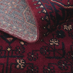 May include: Close-up of a burgundy-colored rug with an intricate pattern. The rug features a detailed design with dark blue and beige accents. The edges are neatly finished, showcasing the rug's quality and craftsmanship.