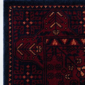 May include: Close-up of a section of a red and navy blue rug with an intricate geometric pattern. The rug has a dark navy blue border and is trimmed with white, red, and navy blue tassels. The design features repeating shapes and floral motifs.