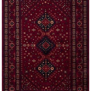 May include: A rectangular, burgundy-colored rug with an intricate geometric pattern. The rug features a central diamond design in black and gold, surrounded by smaller repeating motifs and a fringed border. The overall design is symmetrical and traditional.