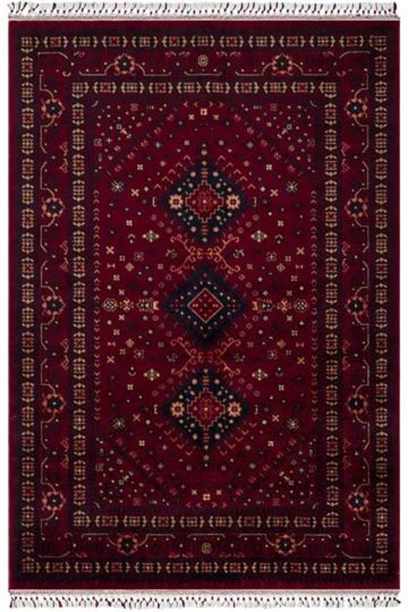 May include: A rectangular, burgundy-colored rug with an intricate geometric pattern. The rug features a central diamond design in black and gold, surrounded by smaller repeating motifs and a fringed border. The overall design is symmetrical and traditional.