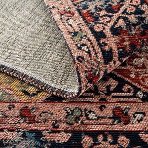 May include: Close-up of a section of a woven rug with a detailed pattern. The rug features a color palette of red, navy blue, and cream. The design includes floral and geometric elements, with a visible textured weave.