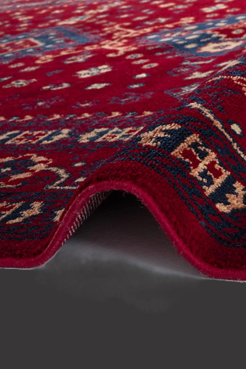 May include: Close-up of a rolled-up red rug with an intricate pattern. The rug features a deep red background with a repeating design in navy blue and beige. The edges are neatly finished, showcasing the rug's texture.