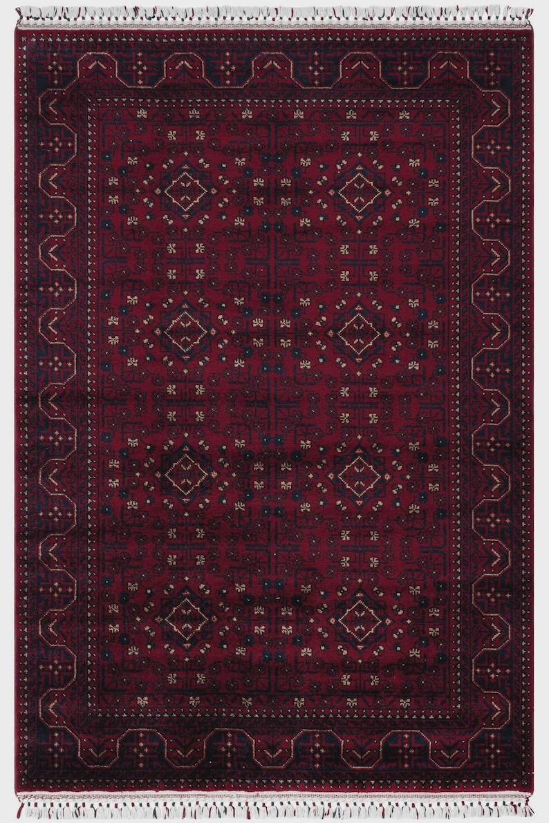 May include: A rectangular, red oriental rug with a detailed geometric pattern. The rug features a central field of repeating diamond and floral motifs in navy and beige, framed by a navy border with a repeating design. The rug has a fringed edge.