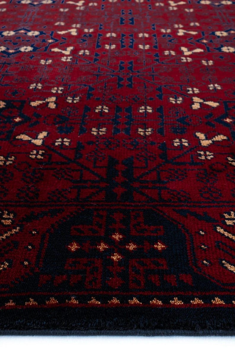 May include: Close-up of a red and navy blue patterned rug. The rug features a repeating geometric design with a dark red background and navy blue and tan accents. The rug's texture is visible.