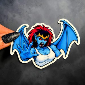 May include: A die-cut sticker featuring a blue-skinned creature with red hair, pointed ears, and sharp fangs. The creature has large blue wings, wears a white tank top, and is reaching forward with a clawed hand. The design includes a gold crown.