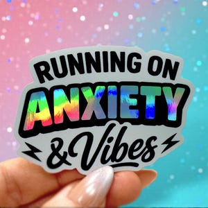May include: A holographic sticker with the text "RUNNING ON ANXIETY & Vibes" in black and rainbow colours. The sticker has a white border and two lightning bolt graphics.