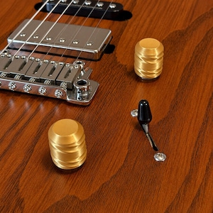 May include: A brown wooden electric guitar body featuring two gold-colored cylindrical control knobs with a spiral texture, a black pickup selector switch, a silver bridge assembly, and a black humbucker pickup with visible metal pole pieces.