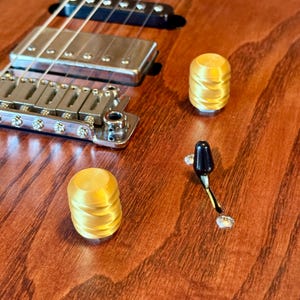 May include: Close-up of a wooden electric guitar with gold-colored knobs and a black tremolo arm. The guitar's hardware is silver, and the wood has a reddish-brown finish.