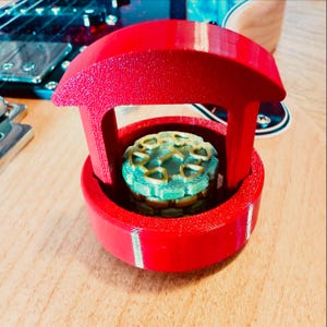 May include: A miniature red wishing well with a green and gold interior. The well has a round base and a curved roof supported by four pillars. The interior features a detailed, layered design.