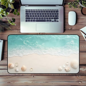 Puede incluir: Alfombrilla de ratón rectangular con una escena de playa: agua turquesa, arena blanca y conchas marinas. La alfombrilla está sobre un escritorio de madera con un portátil, un ratón y pequeñas plantas. Tema costero.