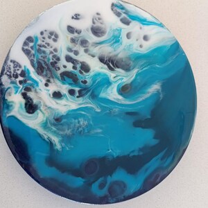 Puede incluir: Obra de arte redonda de resina con un diseño de ola oceánica. La obra presenta tonos de azul y blanco, creando una apariencia dinámica y texturizada. La pieza es un artículo decorativo, adecuado para la decoración del hogar.