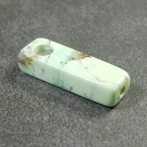 May include: A green and white marbled stone pipe with a small hole on one end and a larger hole on the other end.
