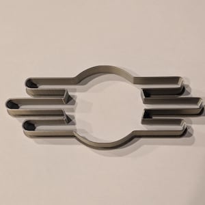 May include: A silver metal cookie cutter in the shape of the Fallout Vault-Tec logo. The logo is a circle with three horizontal lines on each side.