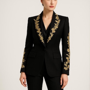 Op de afbeelding: Een zwarte blazer met gouden bloemenborduurwerk op de revers en mouwen. De blazer heeft een klassieke pasvorm met een inkeping in de kraag en twee voorzakken. De broek is zwart.