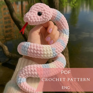 Può includere: Un morbido serpente all'uncinetto a righe rosa, blu e bianche pastello. Il serpente ha occhi neri e una lingua rossa. L'immagine include il testo "PDF CROCHET PATTERN ENG".