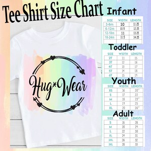 Op de afbeelding: Een wit T-shirt met een regenboog-aquarel achtergrond en de tekst "Hug*Wear" in een zwarte cirkel. Een maattabel voor baby-, peuter-, jeugd- en volwassen maten is inbegrepen met breedte- en lengtemaat in inches.